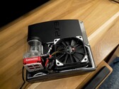 Egyedi vízhűtéses PlayStation 3 egy piros SysCooling szivattyúval és egy nagy fekete ventilátorral a tok belsejében, egy faasztalra helyezve. (Kép forrása: Zac Builds via YouTube)