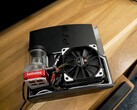 Egyedi vízhűtéses PlayStation 3 egy piros SysCooling szivattyúval és egy nagy fekete ventilátorral a tok belsejében, egy faasztalra helyezve. (Kép forrása: Zac Builds via YouTube)