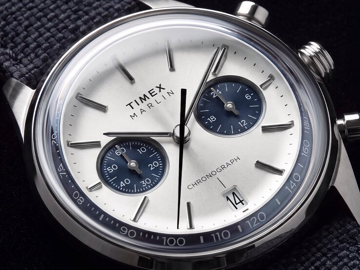 A Timex Marlin Jet Chronograph TW2Y89900 közelképe, amelyen látható az ezüstfehér számlap, a sötétkék kis számlapok, a felragasztott órajelölők, a pálcika alakú mutatók, a tachyméter skála és a dátumablak.