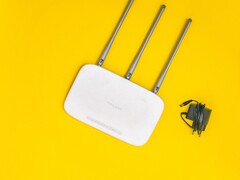 Fehér Wi-Fi útválasztó három antennával és tápegységgel sárga háttér előtt