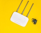 Fehér Wi-Fi útválasztó három antennával és tápegységgel sárga háttér előtt