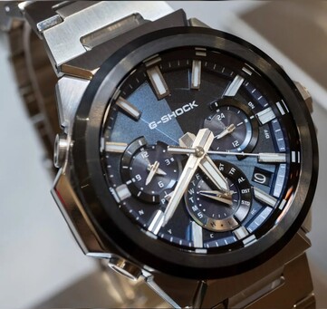 Közelkép a kék számlapos Casio G-Shock GST-W1000AD-2A óráról, amelyen látható a három rétegű kis számlapok elrendezése, a világító jelölések, az ezüst mutatók és a fekete keret.