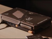 Egy egyedi gyártású, kompakt játékkonzol, amely mini PC-vel, látható hűtőnyílásokkal, USB-portokkal és narancssárga bekapcsológombokkal rendelkezik, az asztalon.