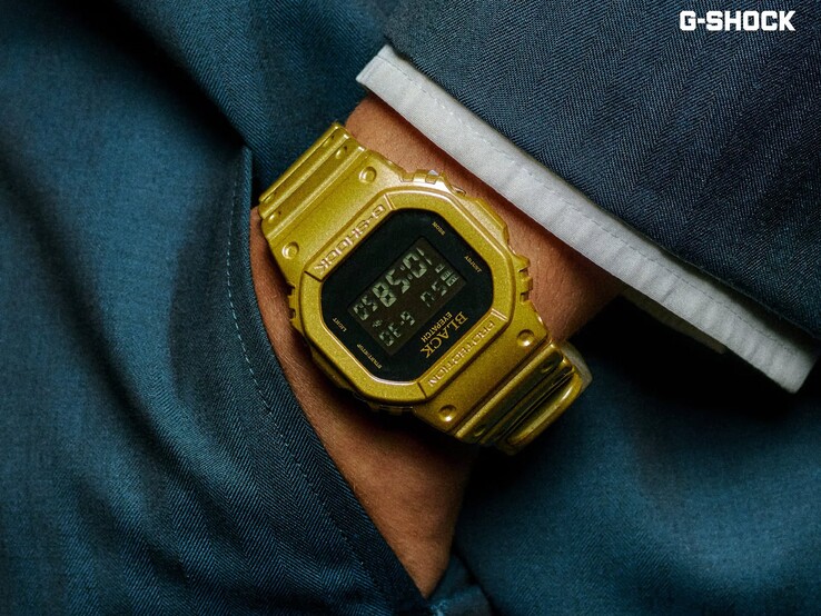 Közelkép egy arany színű Casio G-Shock DW-5600BEP-9 karóráról, amelyet sötétkék szövet előtt viselnek a csuklón. Az óra fekete digitális kijelzővel, arany tokokkal és szíjjal rendelkezik, a kereten és a számlapon pedig a BlackEyePatch márkajelzés látható.