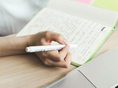 Egy személy jegyzeteket ír egy jegyzetfüzetbe egy nyitott laptop mellett