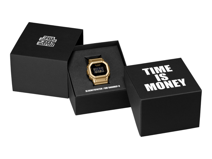 Két fekete díszdoboz között egy arany színű, fekete digitális kijelzős Casio G-Shock DW-5600BEP-9 karóra fekszik. A karóra számlapján a BlackEyePatch márkajelzés látható, míg az előtérben lévő dobozon a „TIME IS MONEY” felirat olvasható.
