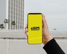 Egy okostelefont tartó kéz, amelynek sárga képernyőjén nagy betűkkel az „eSIM” felirat látható.