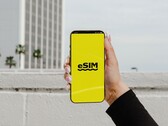 Egy okostelefont tartó kéz, amelynek sárga képernyőjén nagy betűkkel az „eSIM” felirat látható.