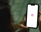 Egy nő, aki mindkét kezében egy okostelefont tart, a kijelzőn az Instagram kezdőképernyője látható