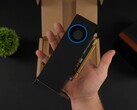 Egy személy kezében az Intel Arc Pro B50 alacsony profilú, fúvóstílusú hűtővel ellátott munkaállomási GPU, a csomagoló dobozával szemben. (Kép forrása: ETA Prime via YouTube)