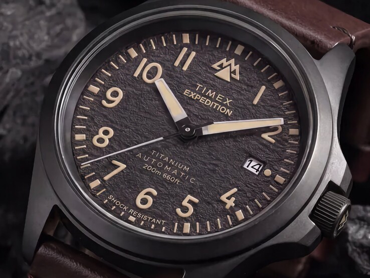 A Timex Expedition Field Post Titanium texturált fekete számlapjának közelképe arab számokkal, világító mutatókkal és jelölőkkel, valamint dátumablakkal.