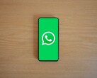 Egy fából készült íróasztalon fekvő okostelefon, amelyen a WhatsApp zöld kezdőképernyője látható a logóval.