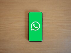 Egy fából készült íróasztalon fekvő okostelefon, amelyen a WhatsApp zöld kezdőképernyője látható a logóval.
