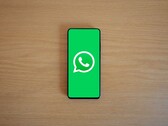 Egy fából készült íróasztalon fekvő okostelefon, amelyen a WhatsApp zöld kezdőképernyője látható a logóval.